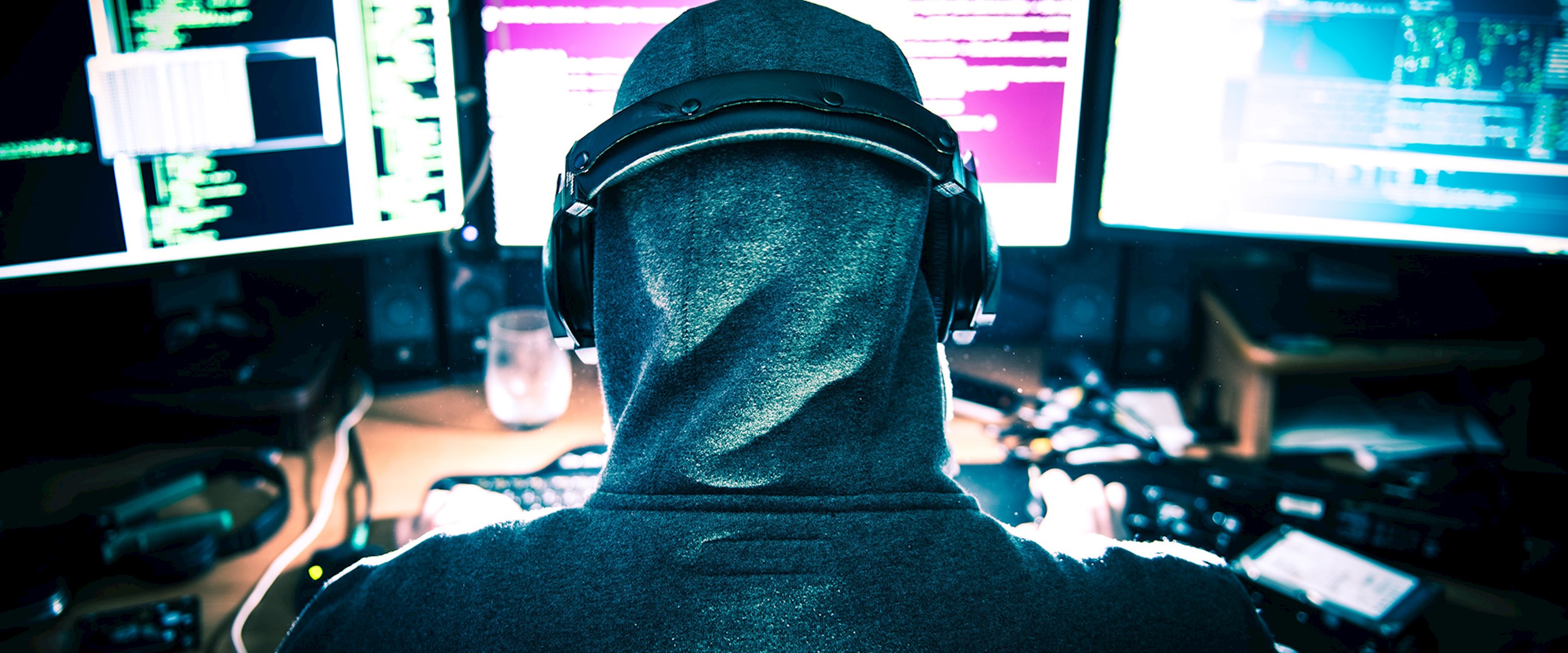 Person in hood in front of computer screens