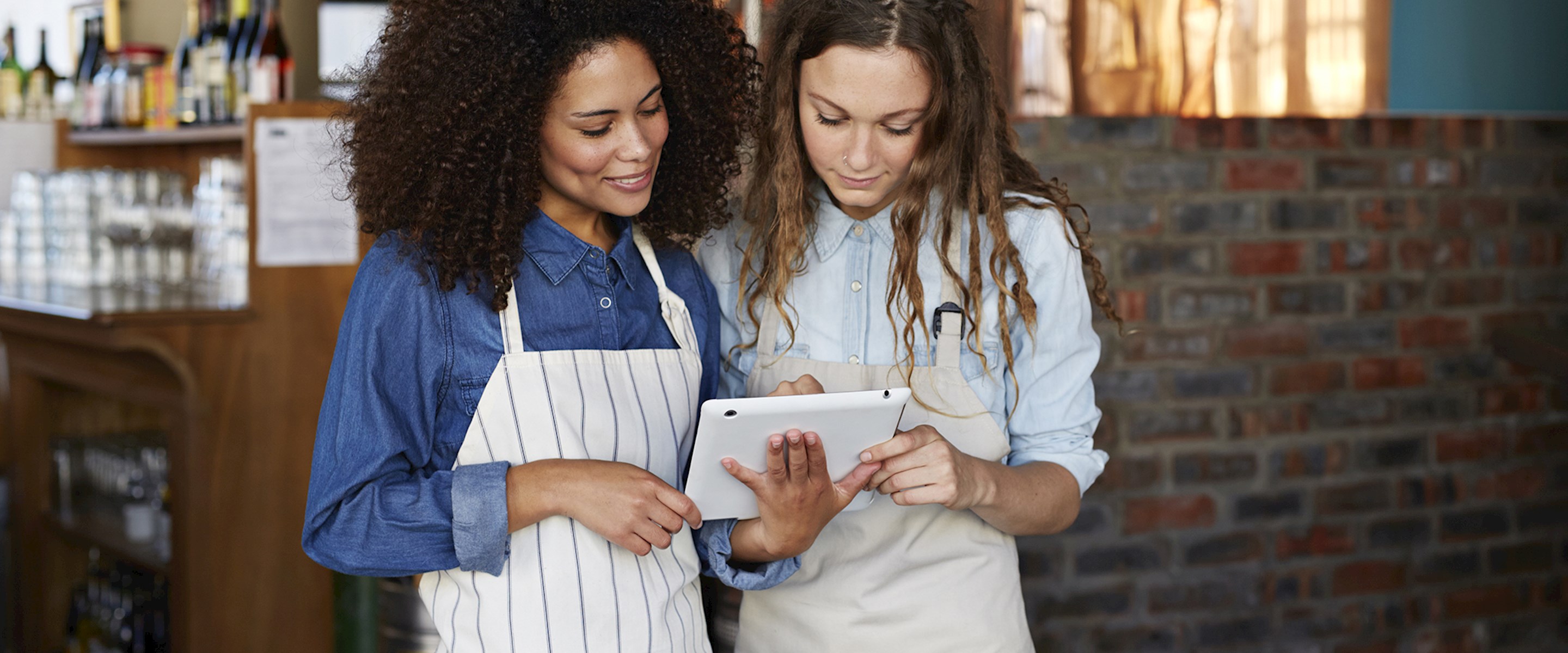 Two women in aprons looking at a tablet