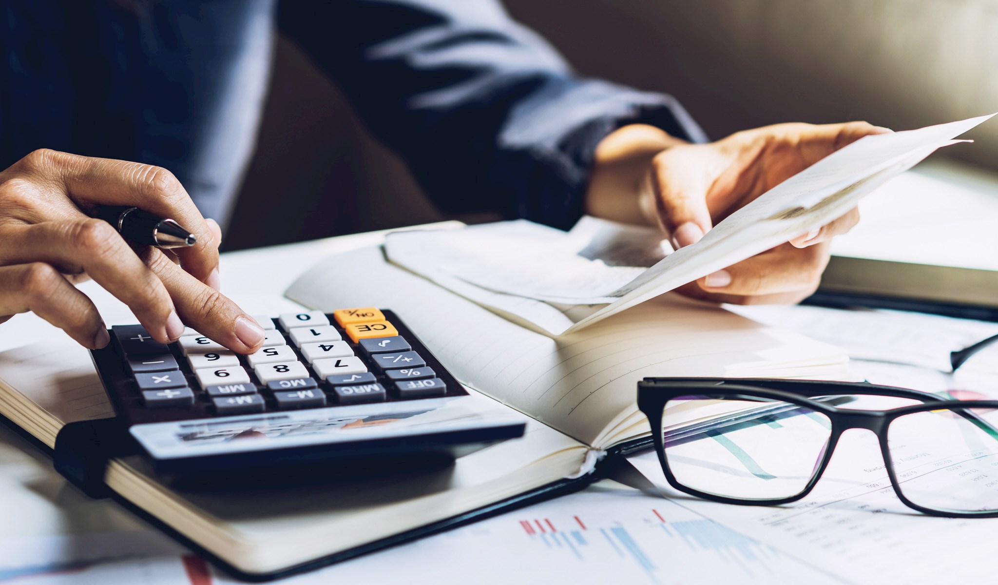 Hand on a calculator on a desk with papers
