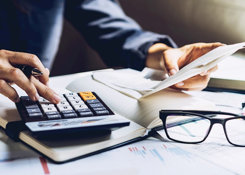 Hand on a calculator on a desk with papers
